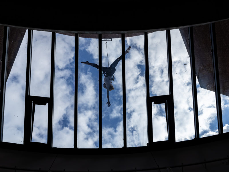 A vertical dance participant does a split jump on a curved wall over a glass roof at ACCA during the Creative Lab